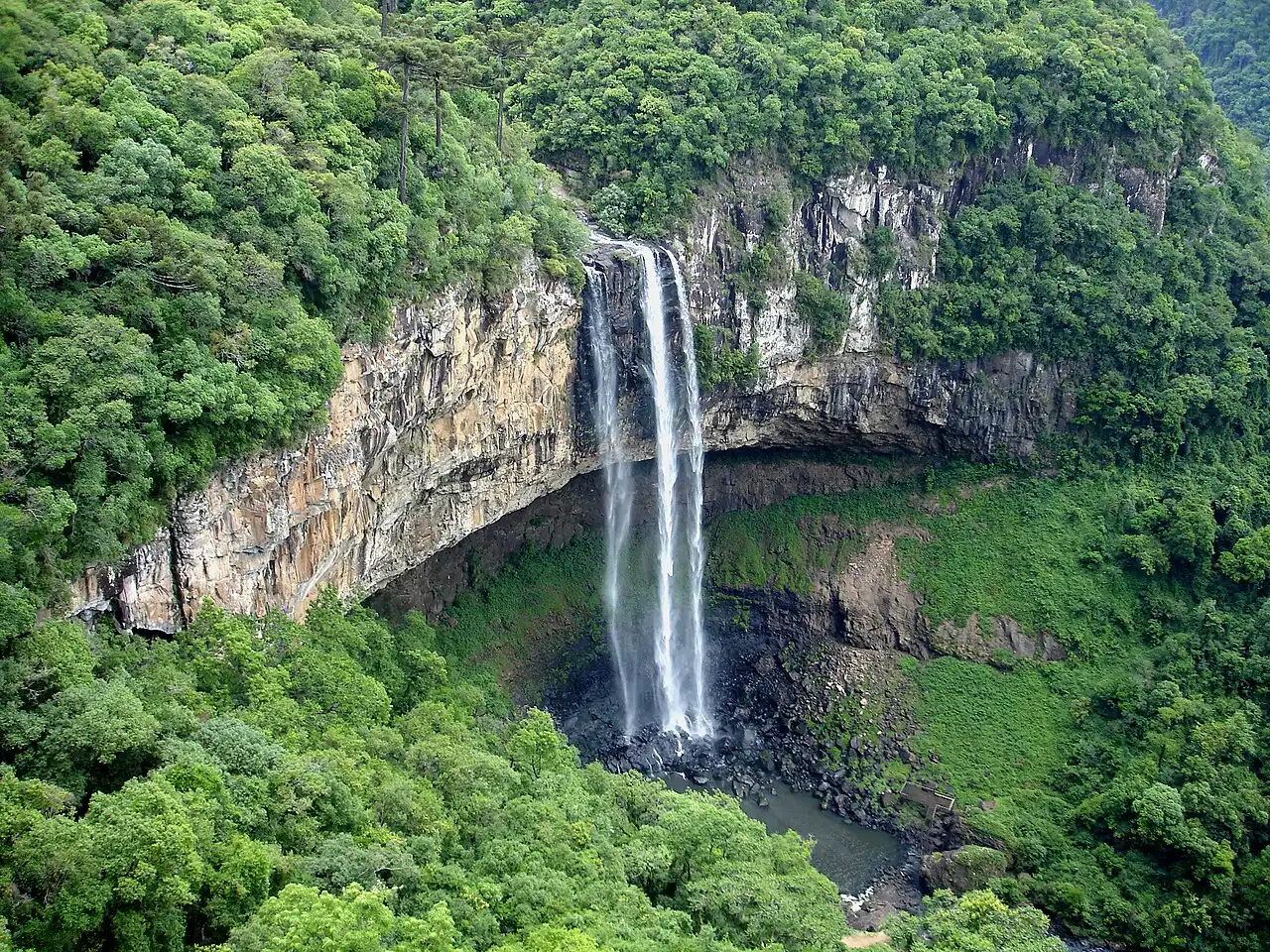 A Cascata do Caracol, em Canela, uma queda d'água alta e estreita que despenca de um paredão de pedra para um vale coberto de mata verde.