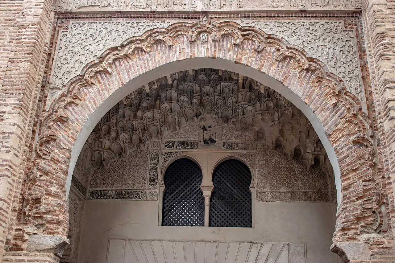 O portal do Corral del Carbón, um arco em ferradura de tijolo com estuque rendado e uma abóbada de muqarnas sobre duas janelas gêmeas.