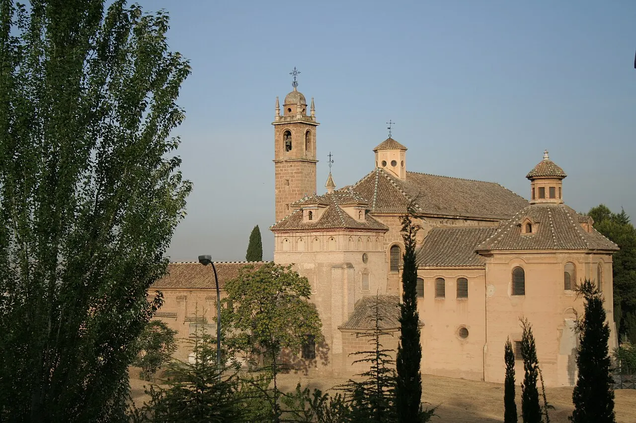 A igreja do Monasterio de la Cartuja, com torre e cúpulas de pedra clara, entre álamos e ciprestes na luz do fim de tarde.