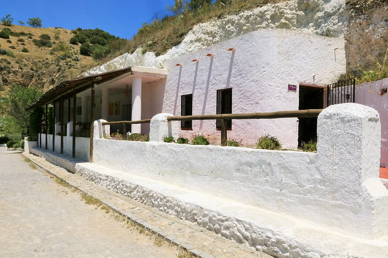 As casas-caverna caiadas do museu do Sacromonte, escavadas na encosta, com uma varanda coberta e um muro baixo branco à frente.