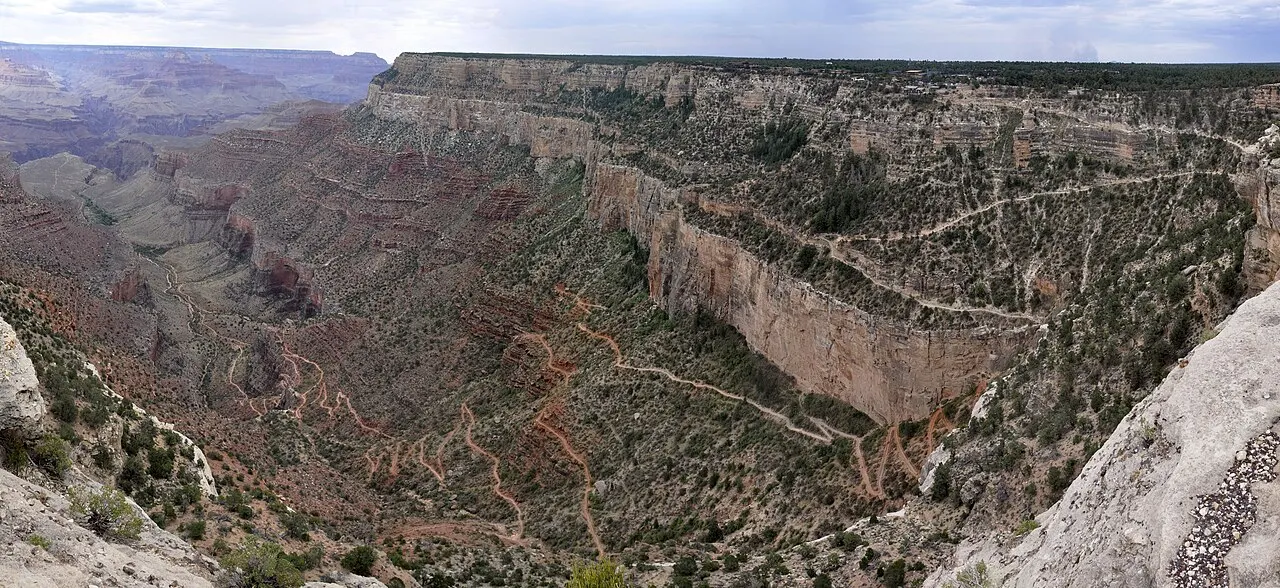 Vista panorâmica de cima do cânion lateral, com a trilha descendo em zigue-zagues pela encosta e paredões claros ao lado.