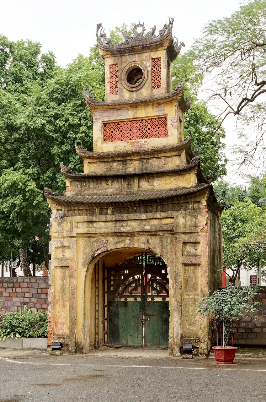 Portão de tijolo com três arcos e uma torre central de dois andares, no fim de um caminho gramado.