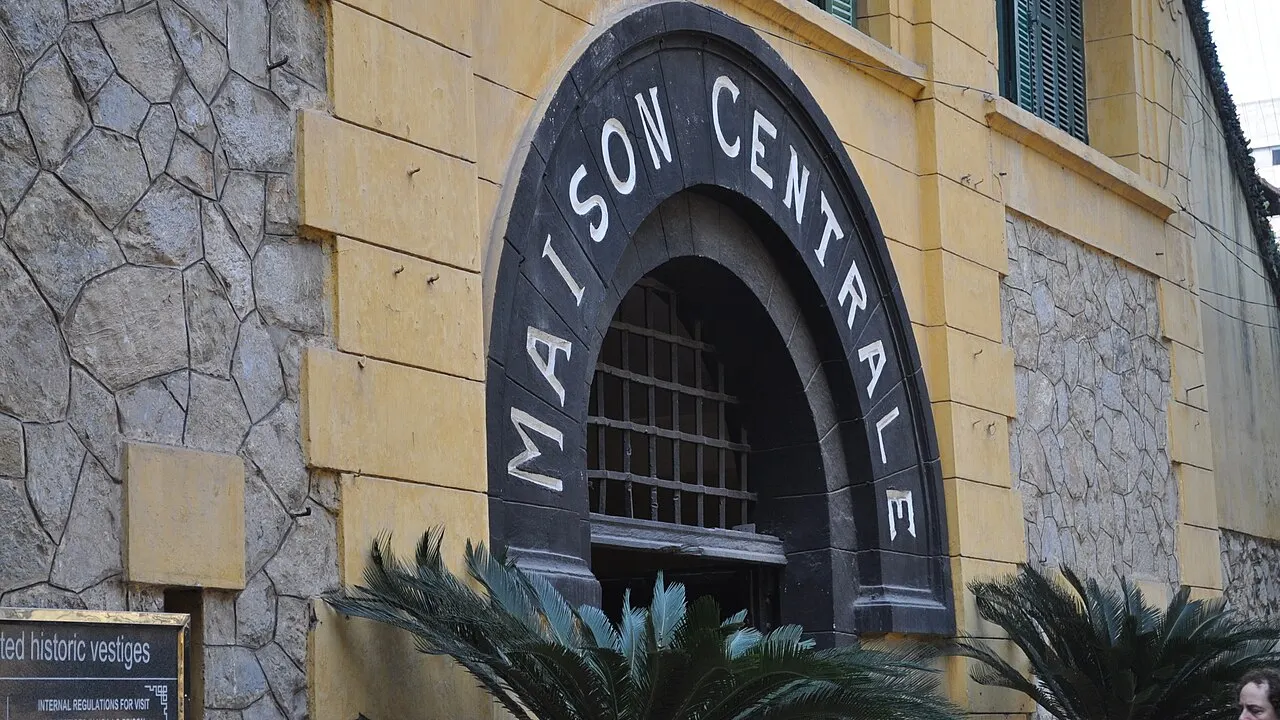 Um arco escuro com as palavras Maison Centrale e uma grade fecha a parede amarela de pedra, com palmeiras baixas na frente.