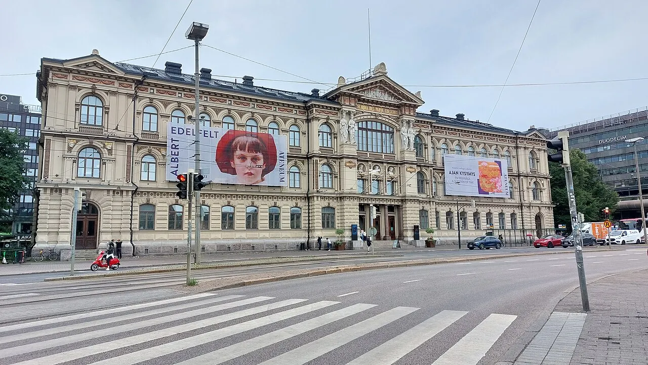 Fachada do museu Ateneum, em Helsinque, com colunas, estátuas no alto e banners vermelhos.