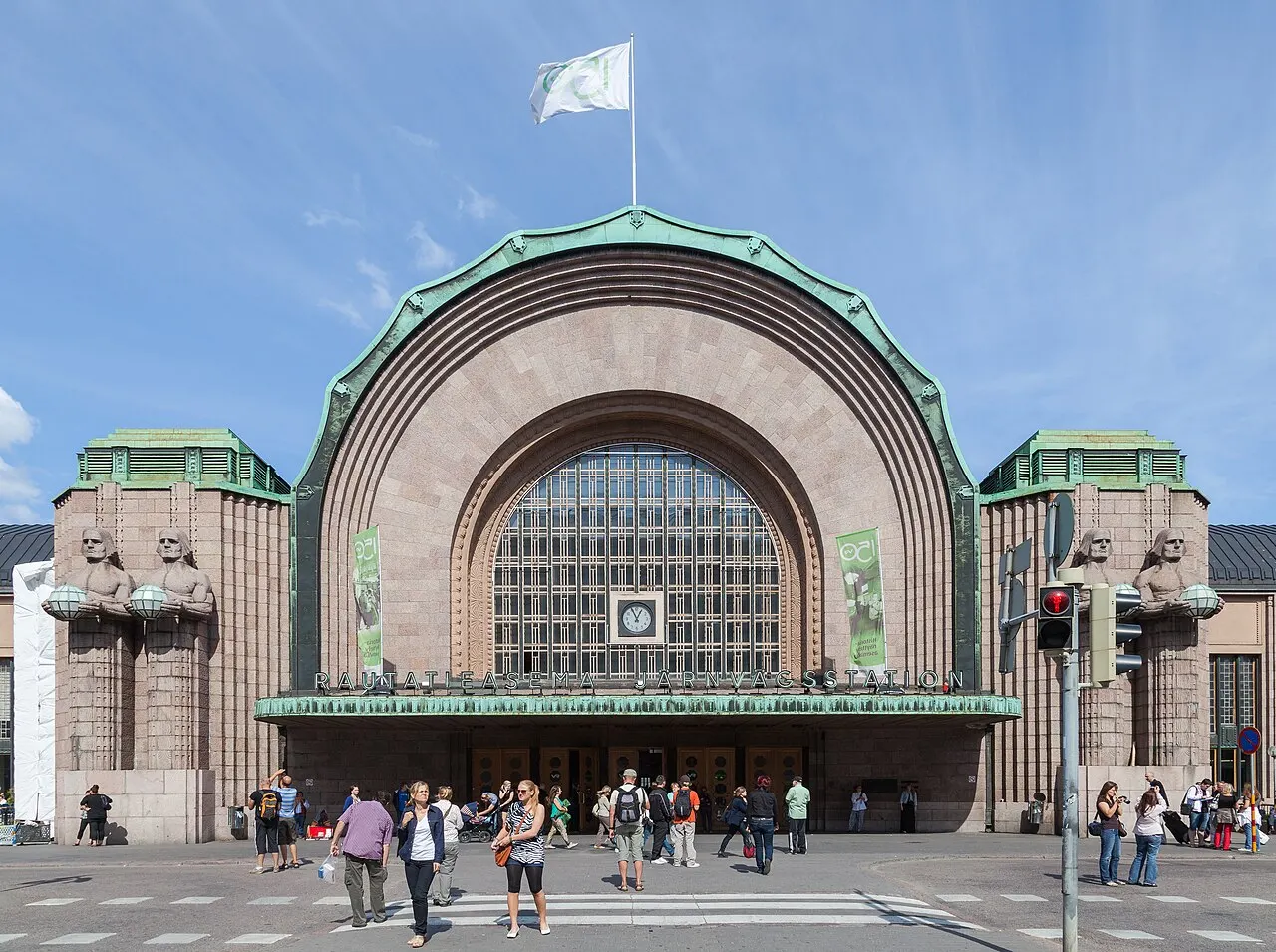Entrada em arco da Estação Central de Helsinque, de granito, com as estátuas que seguram lanternas ao lado.