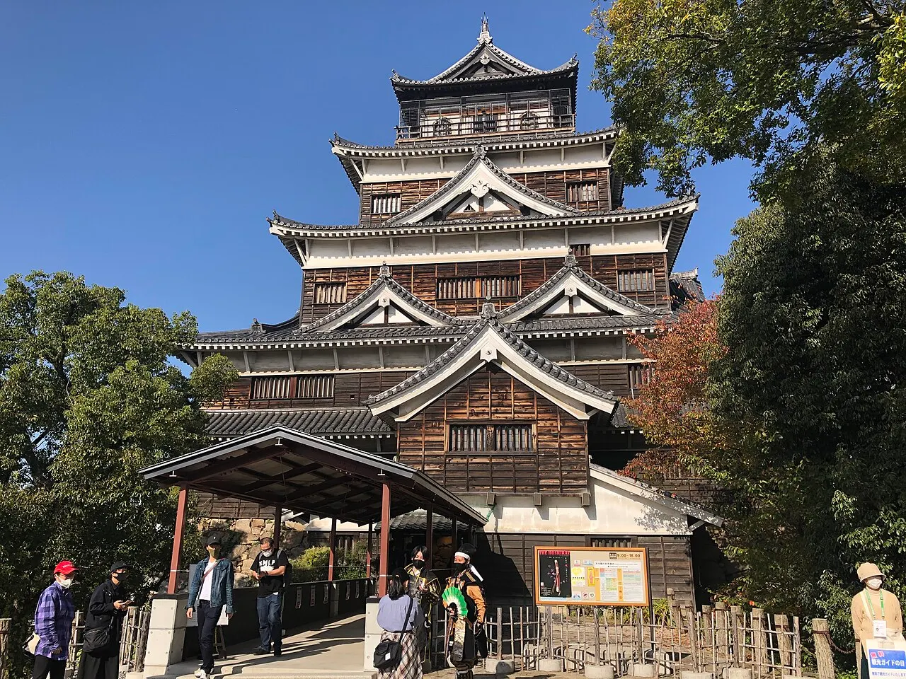 Torre de castelo japonês em cinco andares, de madeira escura e telhados curvos, com árvores ao lado.