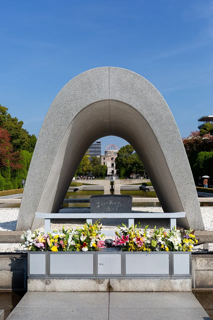 Arco de concreto em forma de sela sobre um baú de pedra com flores, no parque.