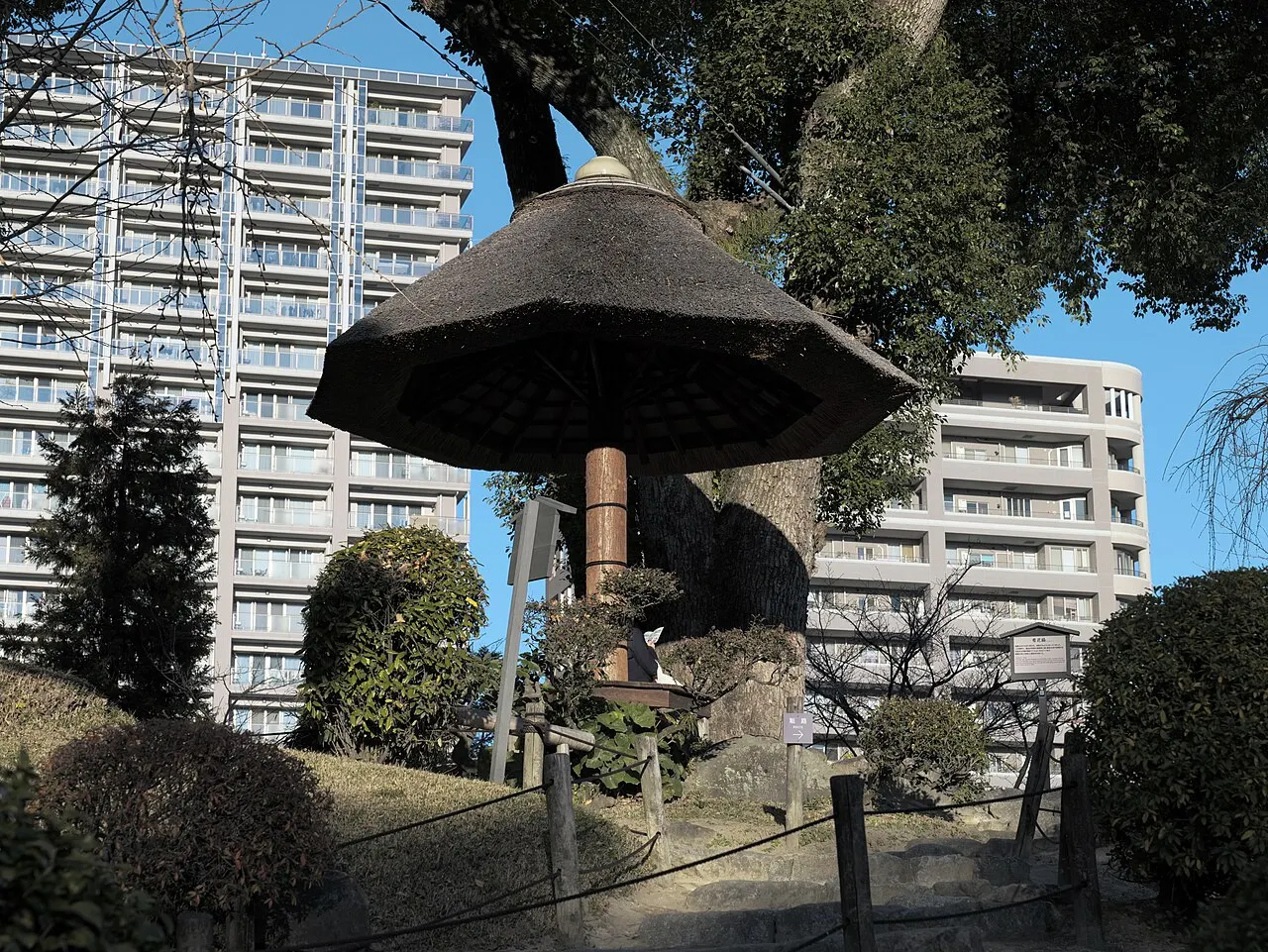 Pequeno abrigo de sapê em forma de guarda-chuva sobre um mastro de madeira, no jardim.