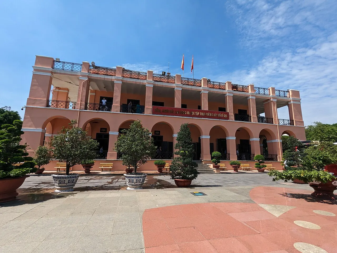 Prédio colonial amarelo de dois andares e telhado marrom, com torre central e arcadas.