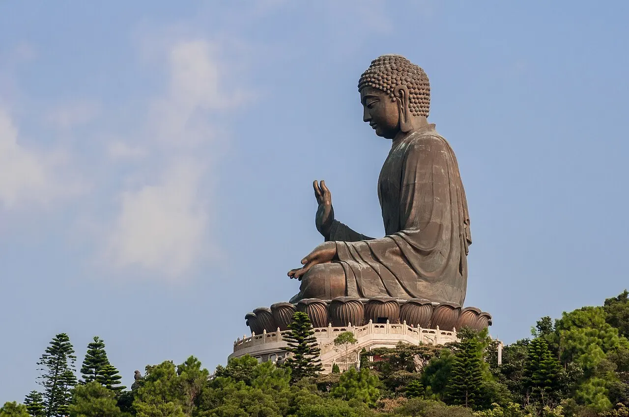 Estátua de bronze de Buda sentado, com a mão erguida, sobre um pedestal no alto do morro.