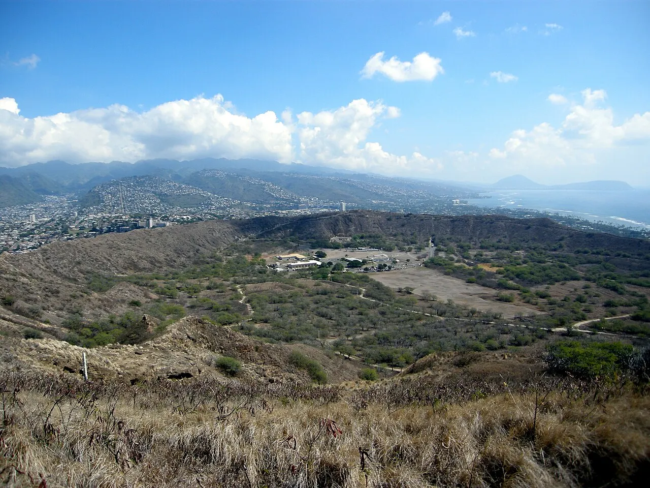O fundo da cratera do Diamond Head visto da borda, com mato seco, trilhas e Honolulu e as montanhas ao fundo.