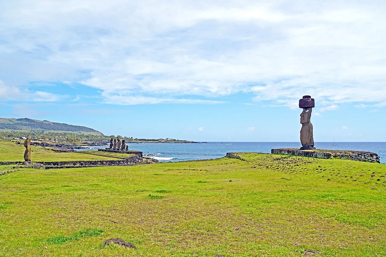 O moai de Ko Te Riku, com o chapéu de pedra vermelha, sobre a plataforma à beira do mar em Tahai, com outros moais e a costa ao fundo.