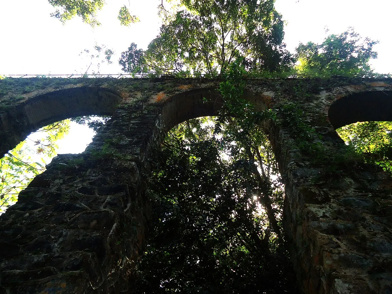 Os arcos de pedra do antigo aqueduto cobertos de musgo, no meio da mata da trilha perto do Abraão.