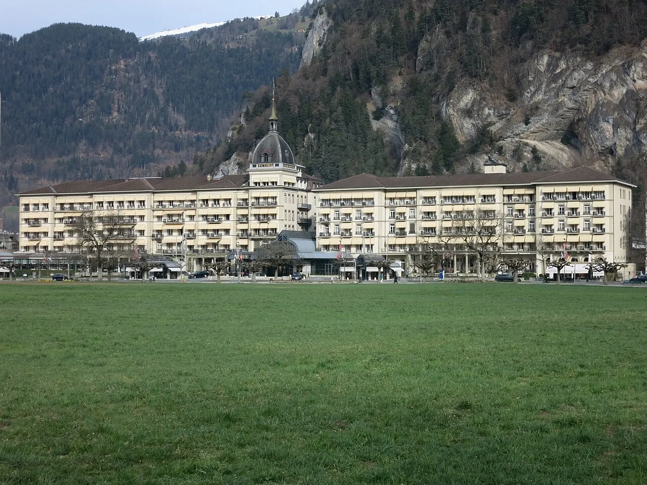 O gramado aberto do Höhematte, no centro de Interlaken, diante da fachada longa do hotel Victoria-Jungfrau e das encostas atrás.