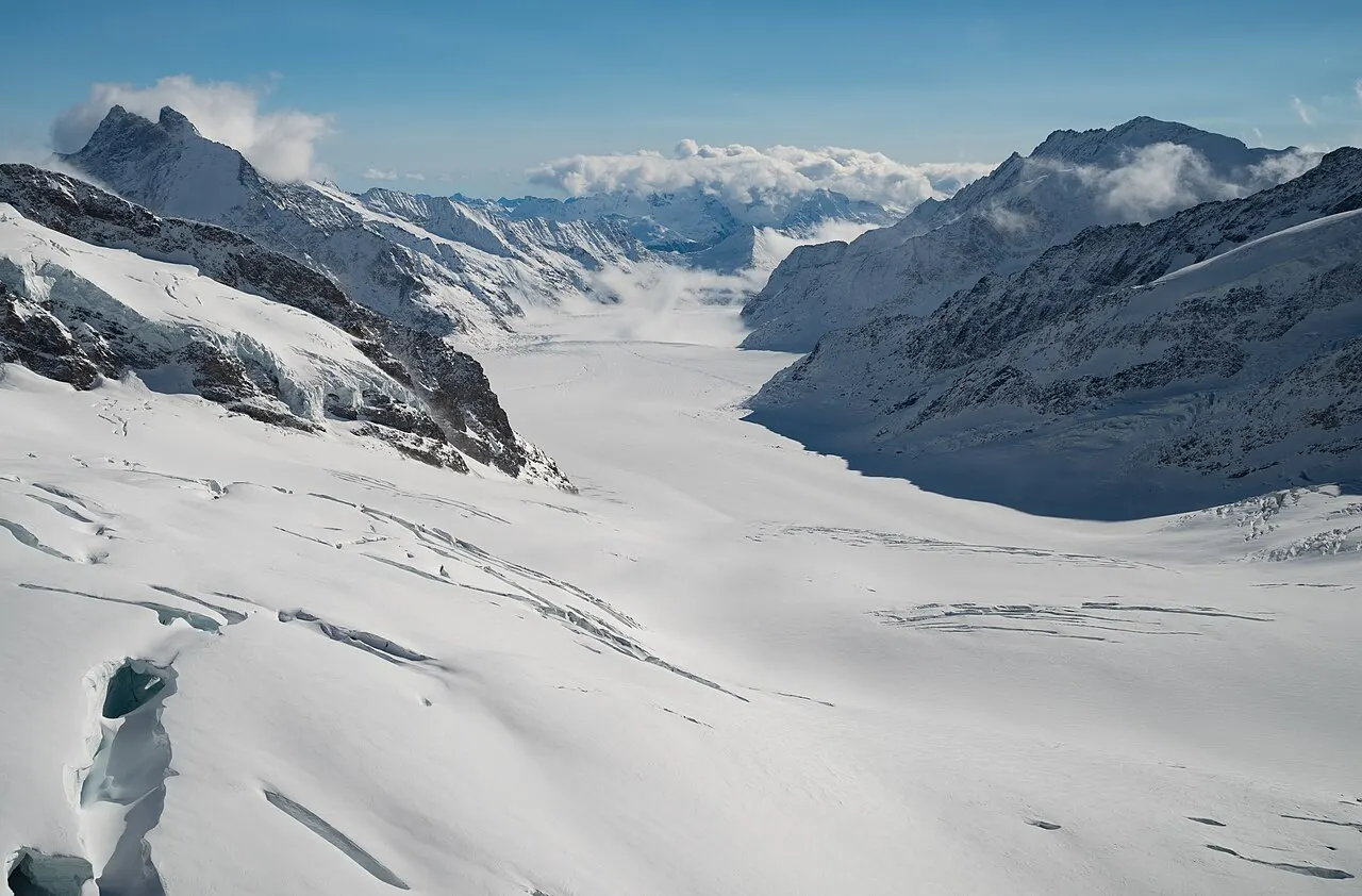 A vista do Jungfraujoch sobre a geleira Aletsch, um rio de gelo branco entre picos rochosos e nevados, sob céu azul.