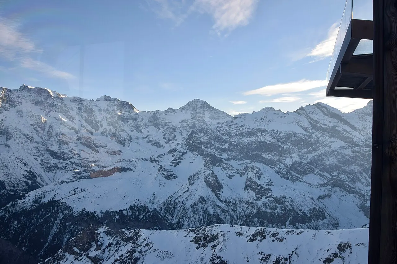 Os picos nevados do vale de Lauterbrunnen vistos da estação do teleférico do Schilthorn, com um pilar escuro à direita.