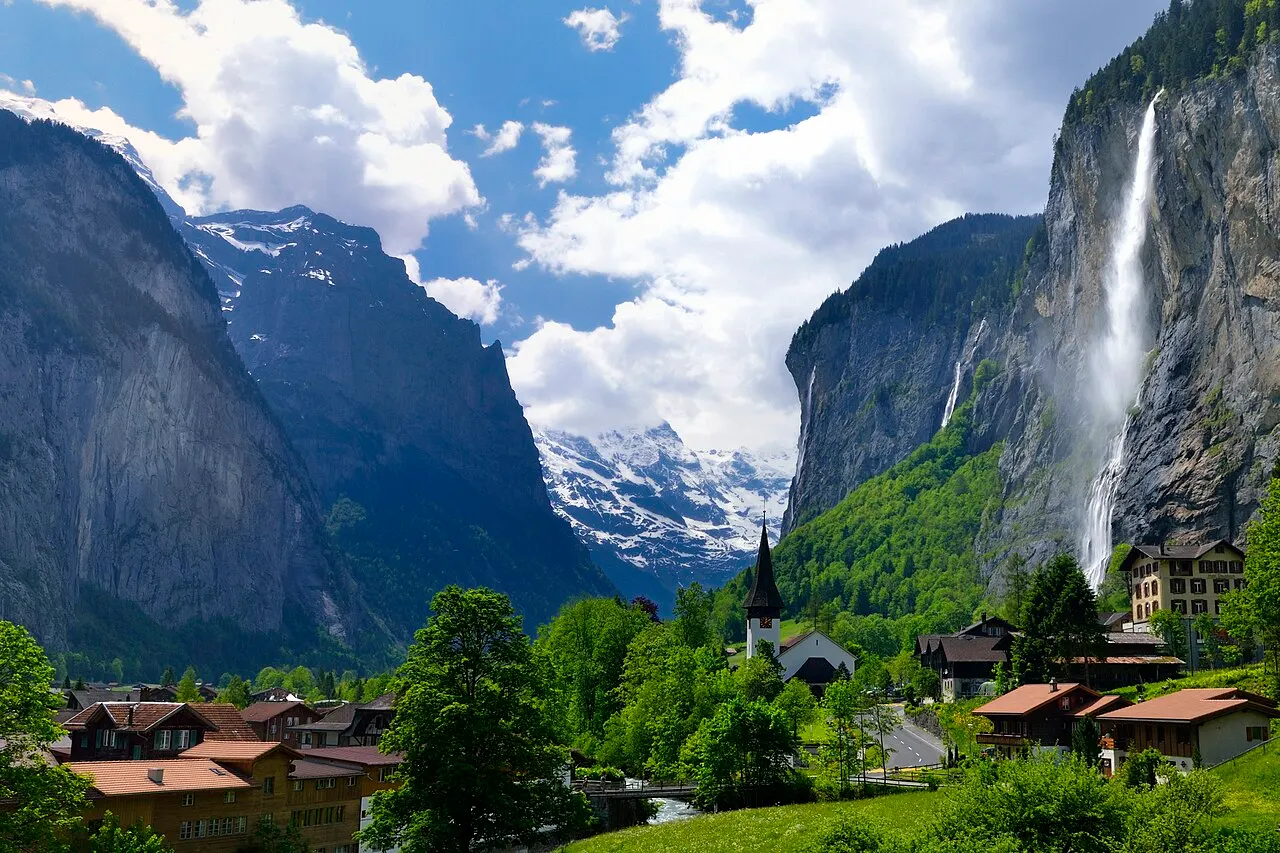 A queda alta e fina do Staubbachfall descendo o paredão de rocha sobre as casas e a igreja de Lauterbrunnen, no vale verde.