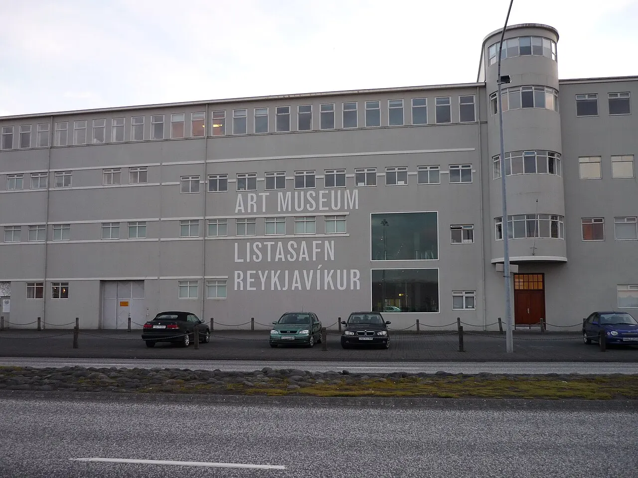 Fachada cinza do Hafnarhús com o letreiro Art Museum e Listasafn Reykjavíkur, a torre de canto e carros estacionados.