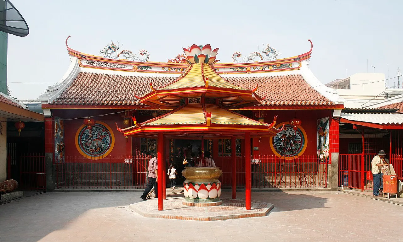 Templo vermelho e dourado com telhado curvo de beiradas erguidas e um incensário à frente.
