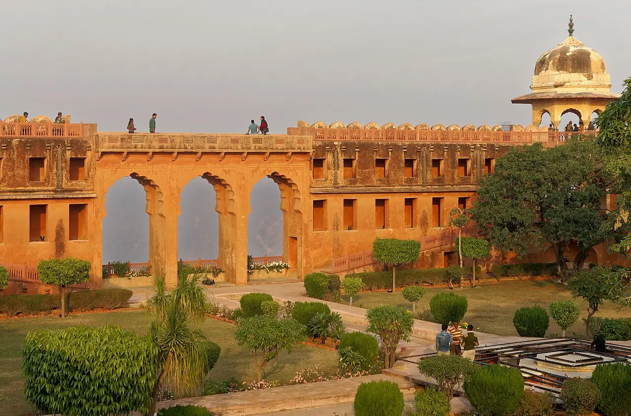 Muralha de arcos do Forte Jaigarh, com jardim na frente, um pavilhão de cúpula e pessoas sobre a muralha.