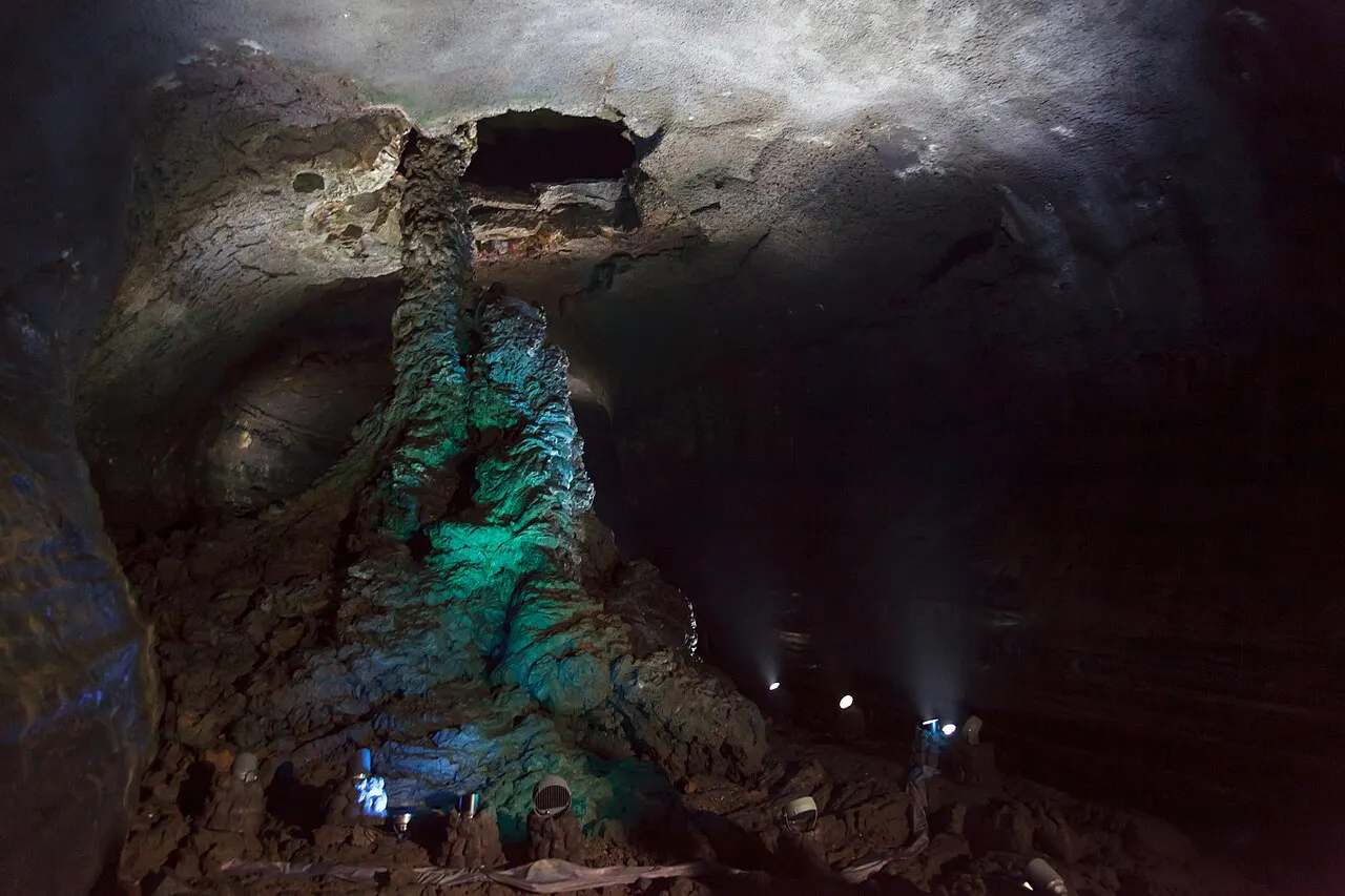 La columna de lava dentro de la cueva de Manjanggul, iluminada en tonos verdes, con el techo de roca oscura del tubo encima.