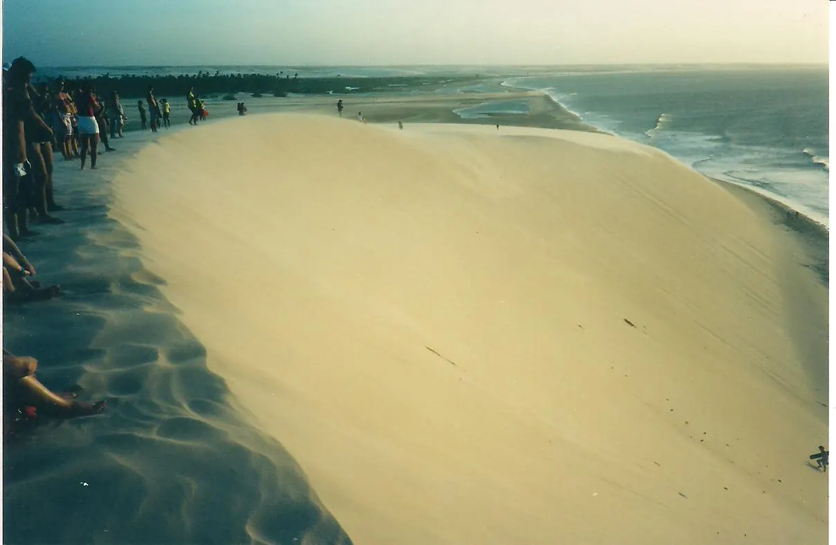 A encosta clara da Duna do Pôr do Sol, em Jericoacoara, com pessoas no alto esperando o pôr do sol e o mar ao fundo, numa foto de cores esmaecidas.