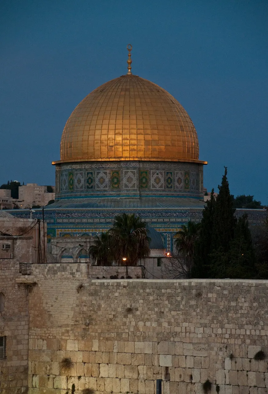 Cúpula da Rocha, dourada, acima do Muro Ocidental de Jerusalém, ao entardecer.