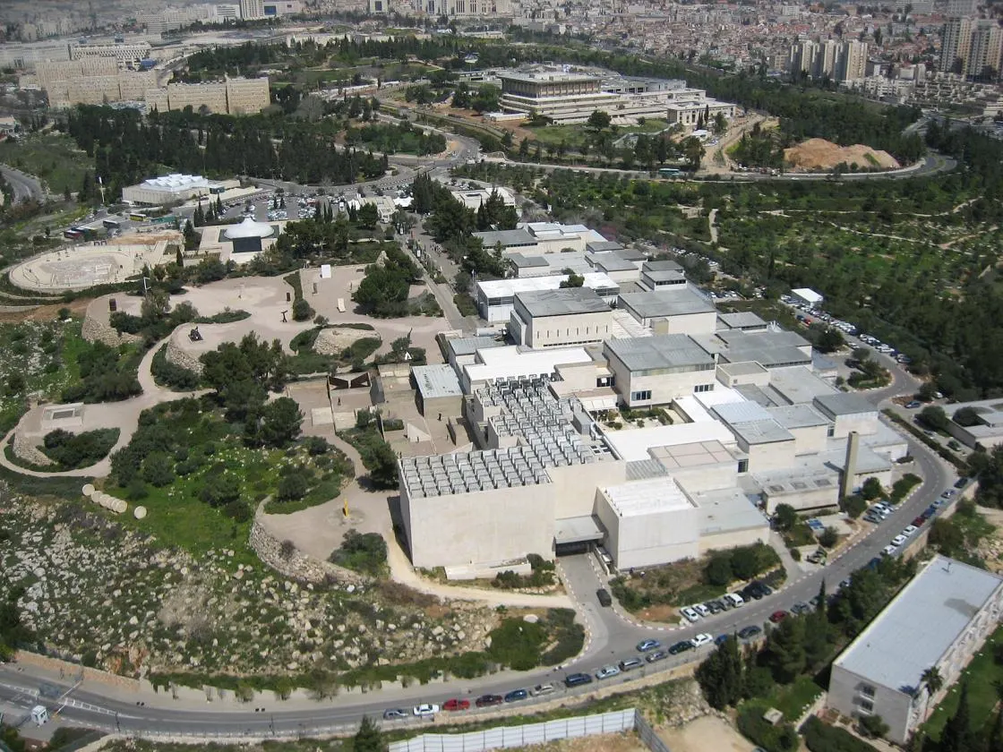 Vista aérea do conjunto de pavilhões baixos e claros do Museu de Israel, com o domo branco do Santuário do Livro à esquerda e a cidade ao fundo.