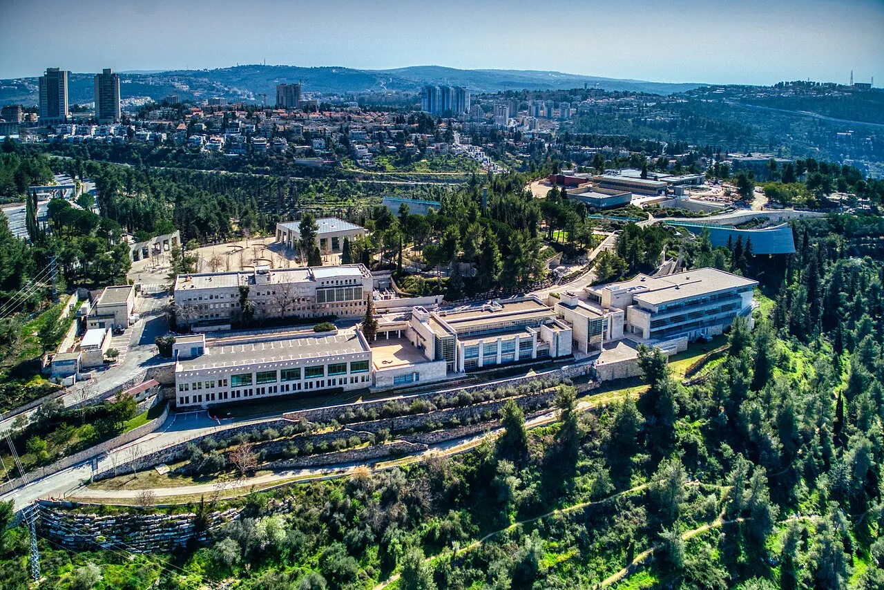 Vista aérea do Yad Vashem, com prédios brancos entre pinheiros e a cidade nas colinas ao fundo.