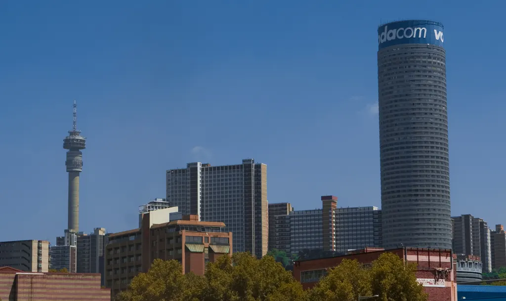 Torre cilíndrica da Ponte City ao lado da torre fina de Hillbrow, com outros prédios no meio.
