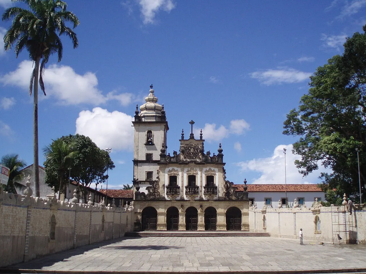 A fachada barroca da igreja e do convento de São Francisco, com a torre e o adro de pedra na frente, sob céu azul.