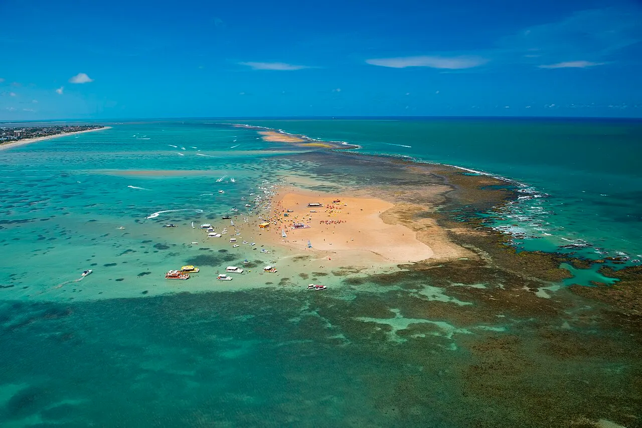 O banco de areia de Areia Vermelha visto do alto, no meio do mar verde-claro, com os recifes em volta.