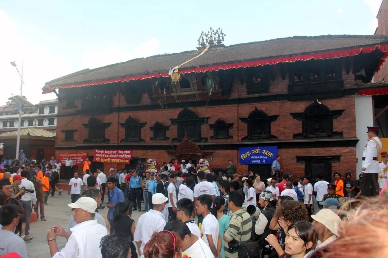 Kumari Ghar de tijolo, com janelas escuras e um ornamento no telhado, e uma multidão na frente.