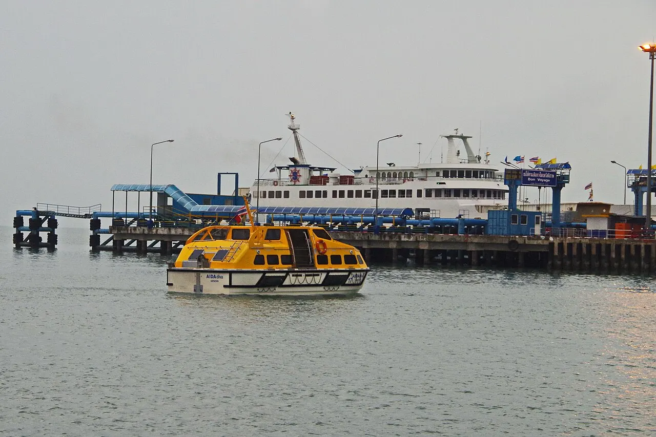 Le quai du port de Nathon avec un ferry blanc à quai et un bateau jaune et noir qui passe devant, sous un ciel gris.