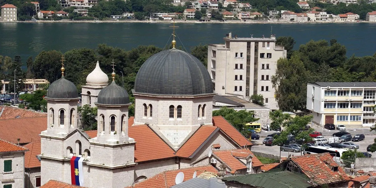 As cúpulas cinzentas e as duas torres da Igreja ortodoxa de São Nicolau vistas do alto, com os telhados da cidade e a baía atrás.