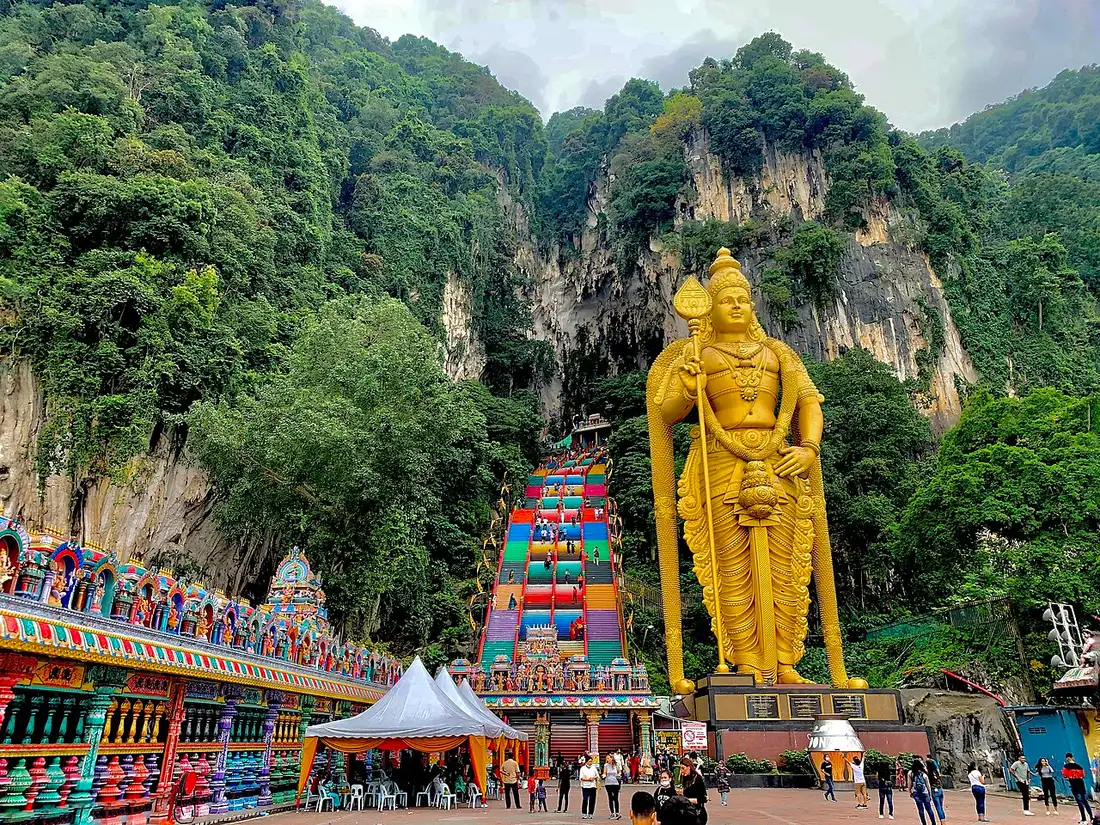 Estátua dourada gigante de uma divindade de pé com uma lança, diante da encosta de calcário.