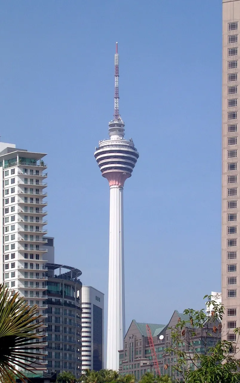 Torre branca e fina com um bulbo de observatório perto do topo e antena, entre prédios.