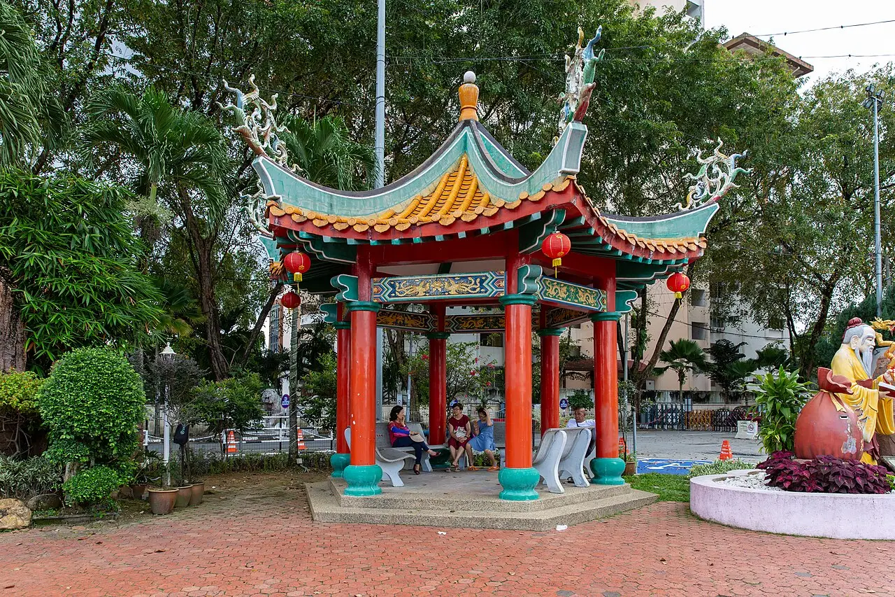 Pavilhão chinês de colunas vermelhas e telhado curvo decorado, num jardim.