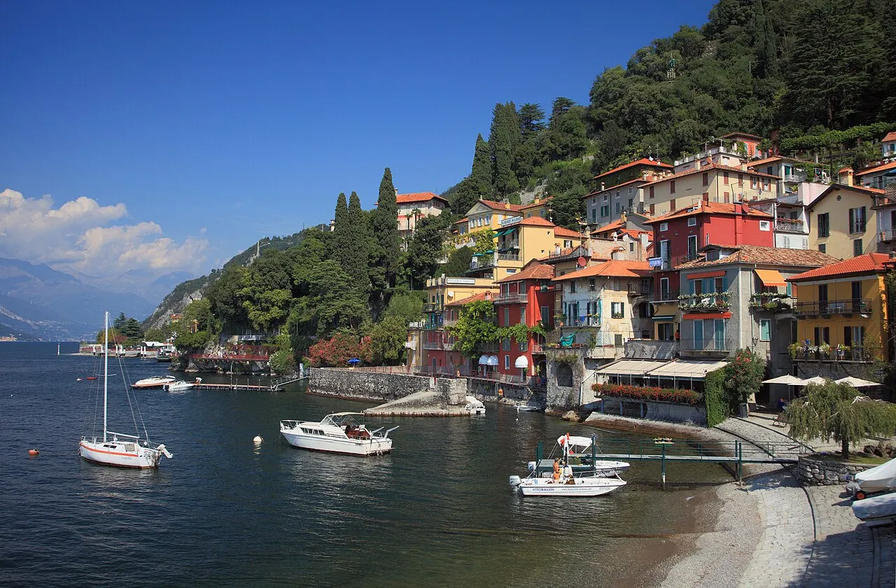 As casas coloridas de Varenna empilhadas na encosta sobre a água, com barcos ancorados e uma pequena praia de pedrinhas.