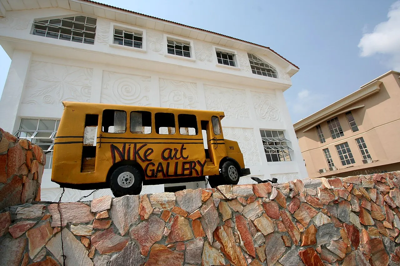 Ônibus amarelo com o nome Nike Art Gallery diante do prédio branco de relevos.
