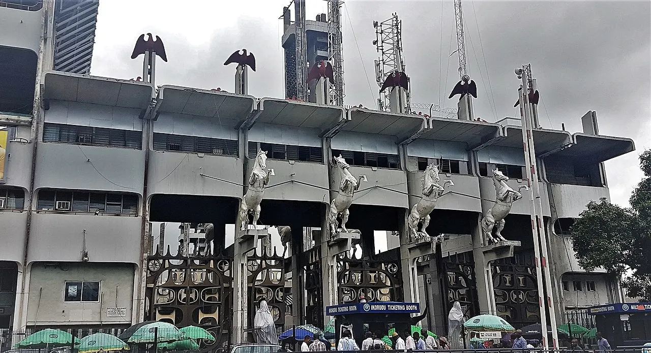 Portão da Tafawa Balewa Square, com estátuas de cavalos brancos e águias, e guarda-sóis verdes embaixo.