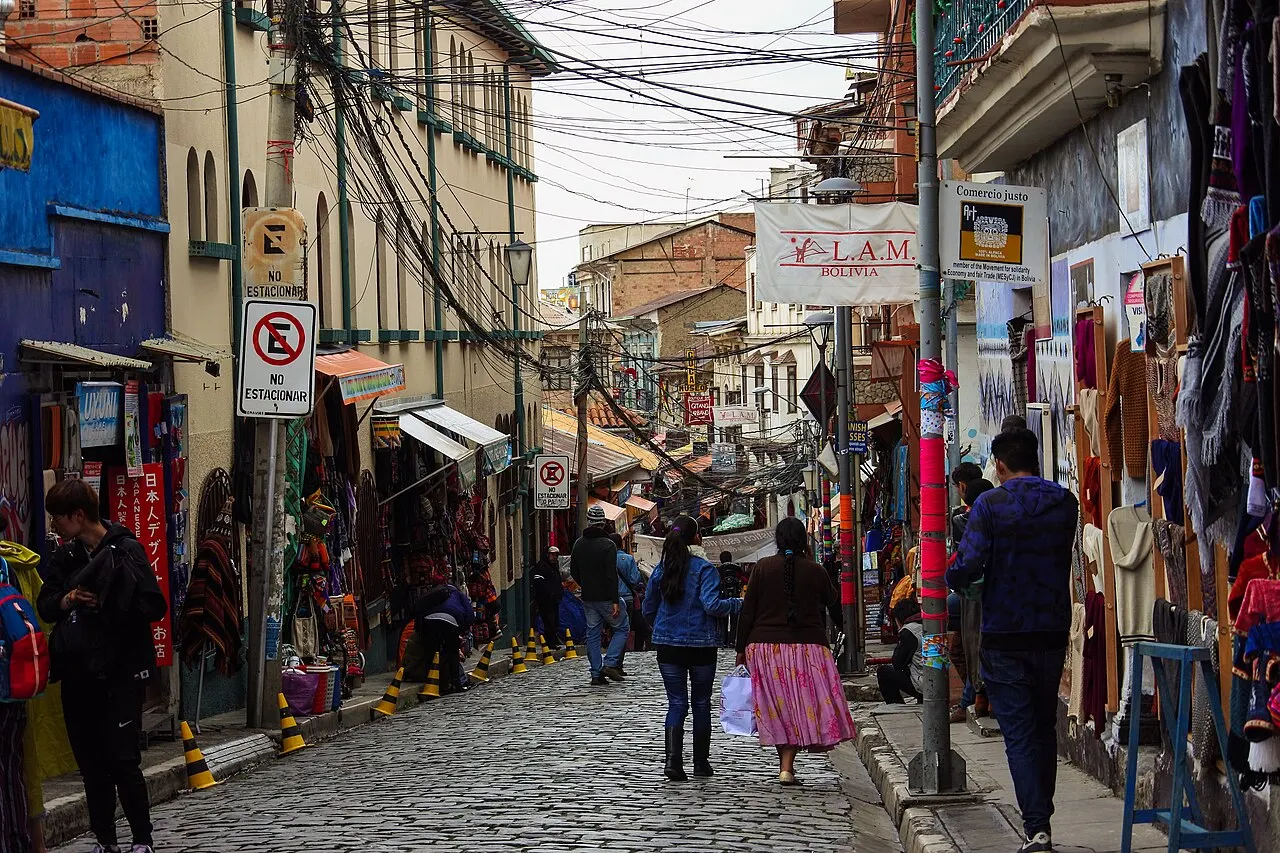 Rua de pedra do Mercado de las Brujas, com lojas, tecidos pendurados e fios sobre a calçada.