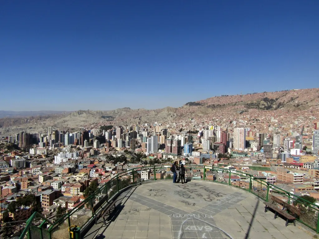 Terraço do Mirador Killi Killi, com grade verde, e La Paz espalhada no vale entre os morros.