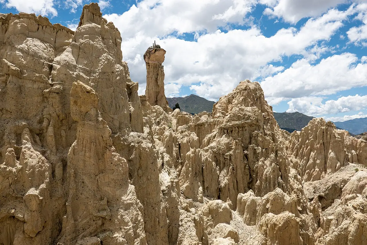 Torres de argila erodida do Valle de la Luna, com um pináculo alto no centro e montanhas ao fundo sob céu azul.