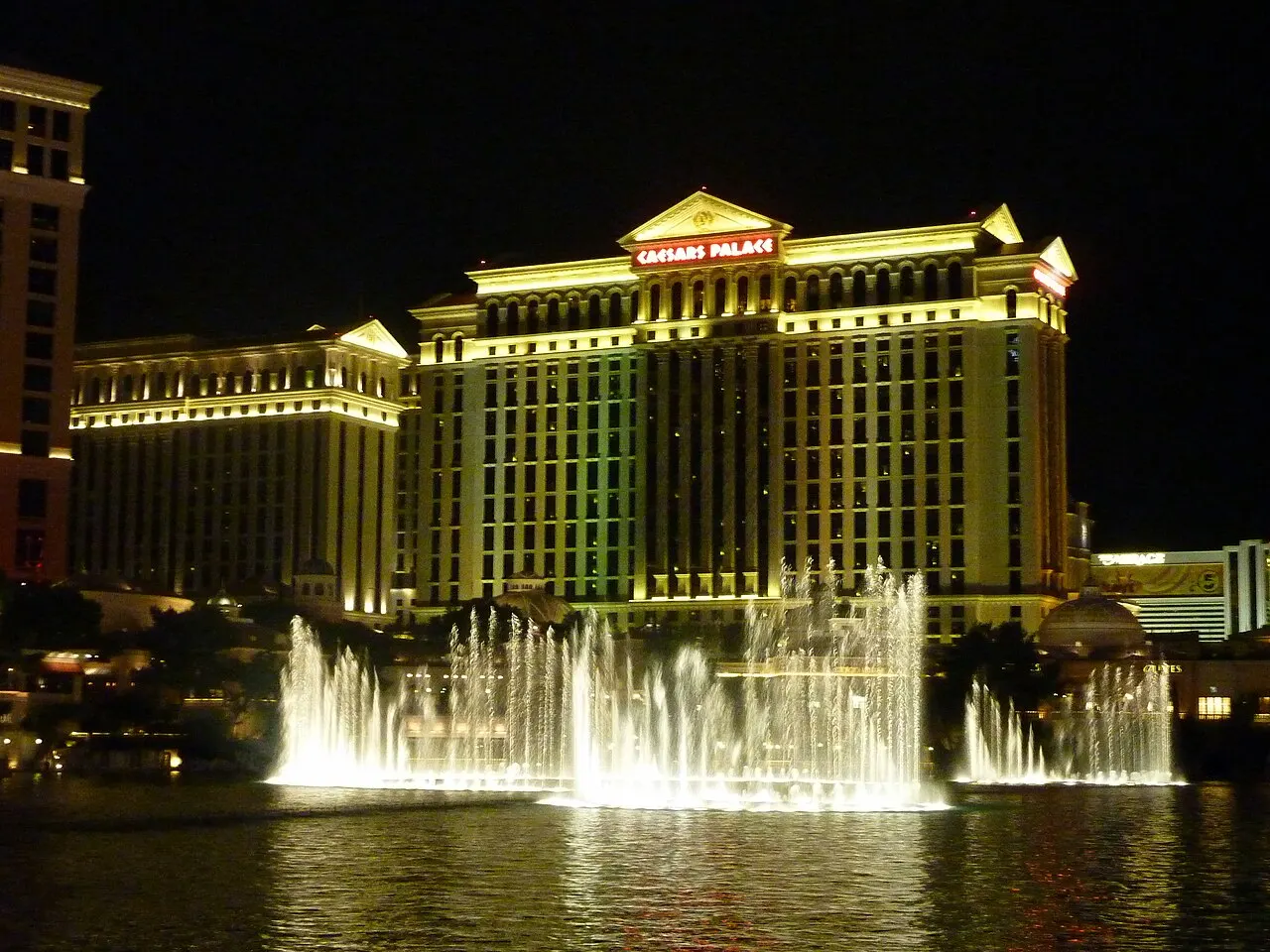 Os jatos das fontes do Bellagio se erguem à noite, em Las Vegas, com o Caesars Palace iluminado ao fundo.