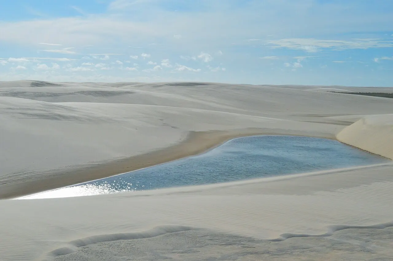 Dunas claras com uma lagoa rasa refletindo o céu, perto de Atins, na ponta dos Lençóis Maranhenses.