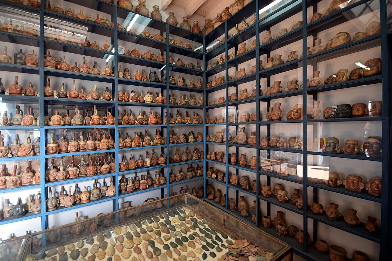 Sala de reserva aberta do Museo Larco: prateleiras de metal azul do chão ao teto, em duas paredes, cheias de vasos de cerâmica pré-colombiana, entre eles vasos-retrato, com uma vitrine de pontas de pedra no centro.