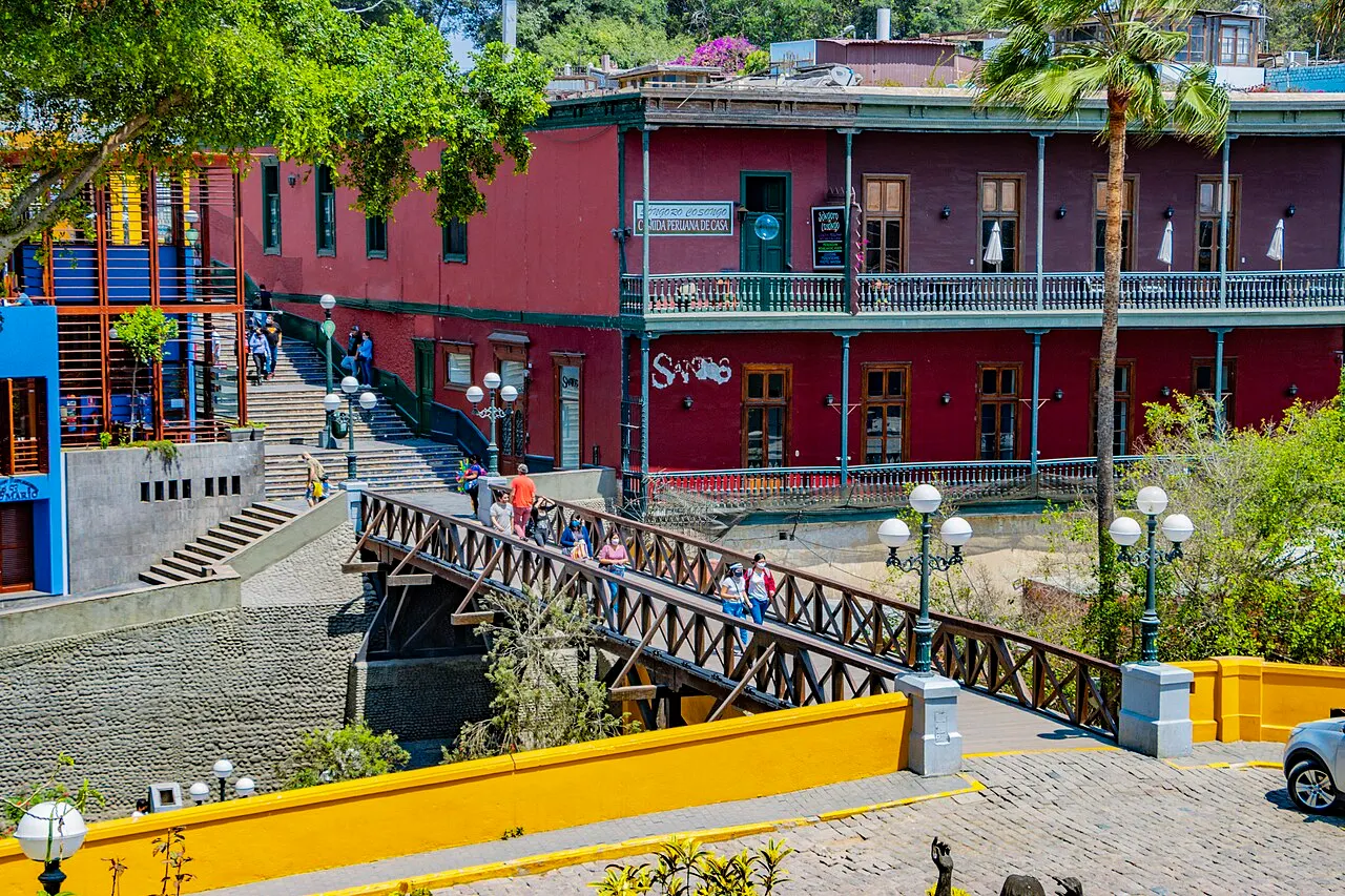 Puente de los Suspiros de madeira, com pessoas na ponte, a casa vermelha atrás e o muro amarelo.