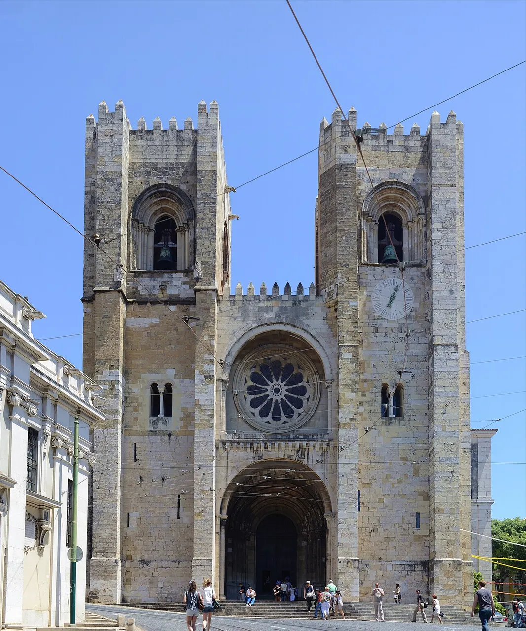 Fachada principal da Sé de Lisboa, com as duas torres de ameias e a rosácea, sob céu azul.