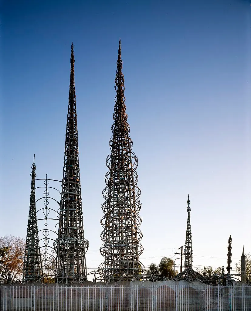 Torre de Watts, em Los Angeles, estrutura afilada de aço coberta de cacos de louça e vidro, sob céu azul.
